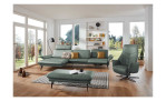 Komfort-Ecksofa 1928 in der Farbausführung grün mit Dekokissen, einem Hocker und einem Sessel im Raum stehend, Sitztiefenverstellung im rechten Element