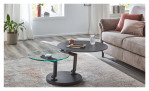 Couchtisch MONDO Varium mit einer Glas-Keramik Tischplatte in Marmoroptik Marquina und einer Klarglasplatte mit einem schwarzen Stahlgetsell. Auf einem dekorierten Hintergrund.