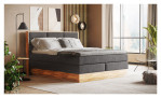Boxspringbett VALMONDO Incana in einem Stoffbezug in Dark Grey und einem Sichtholzrahmen in Eiche. Auf einem dekorierten Hintergrund