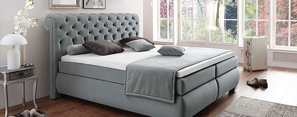 luxuriöses, blau-graues Boxspringbett mit geschwungenem Kopfteil in Chesterfieldoptik