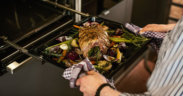 Backblech mit Essen in einen Neff Backofen schieben Backblech mit Essen in einen Neff Backofen schieben
